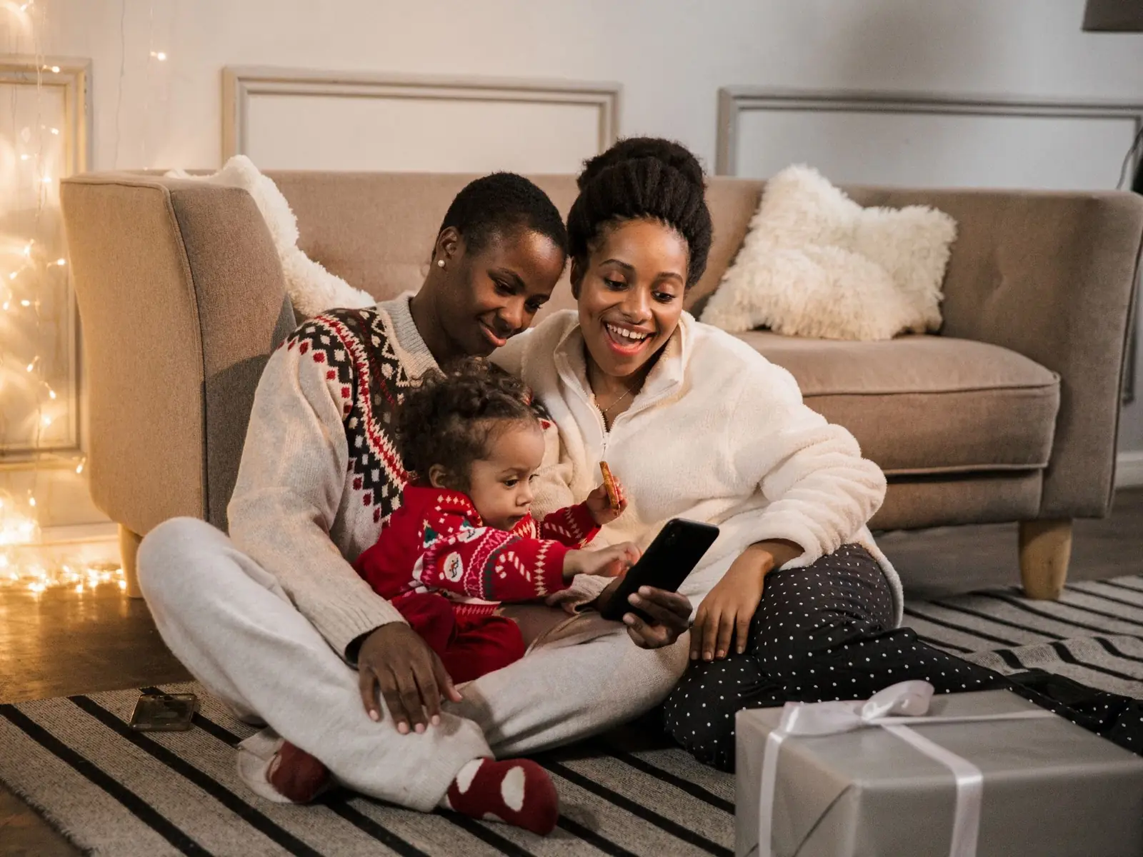 Two adults and a child sitting on the floor and looking at a phone
